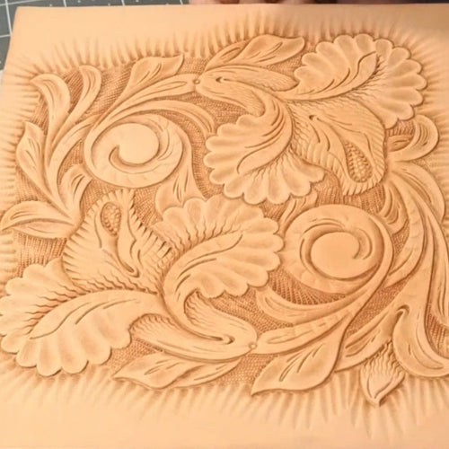 Decorative leather panel with intricate floral patterns on a cutting mat.